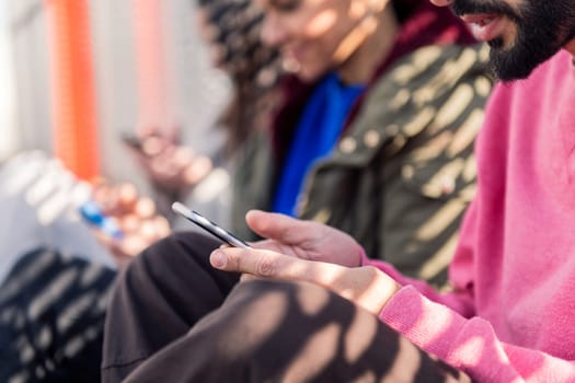 close up of an unrecognizable young man using mobile phone with friends, focus on the hands, concept of technology of communication and modern lifestyle, copy space for text