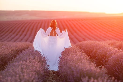 Happy woman in a white dress and straw hat strolling through a lavender field at sunrise, taking in the tranquil atmosphere