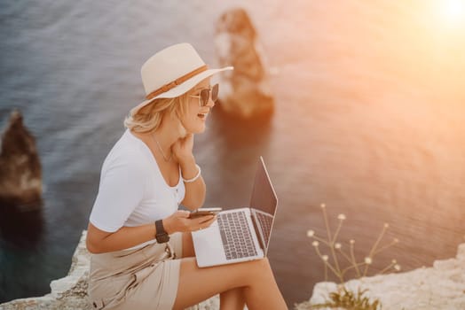 Freelance women sea working on the computer. Good looking middle aged woman typing on a laptop keyboard outdoors with a beautiful sea view. The concept of remote work