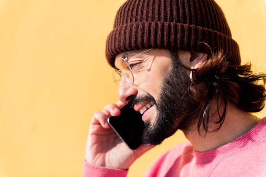 smiling young man talking on mobile phone in a yellow background, concept of technology of communication and modern lifestyle, copy space for text