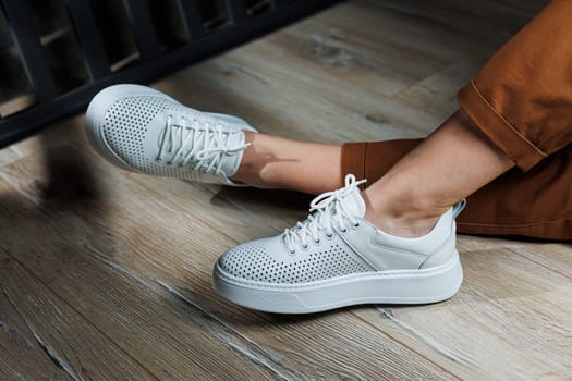 Female legs in white leather sneakers with perforations. Collection of summer women's shoes. White women's sneakers with laces