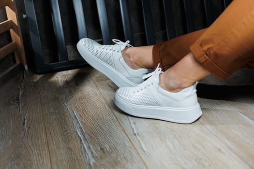 Female legs in white leather sneakers with perforations. Collection of summer women's shoes. White women's sneakers with laces