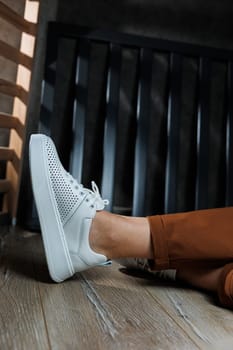 Female legs in white leather sneakers with perforations. Collection of summer women's shoes. White women's sneakers with laces