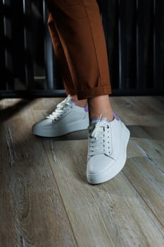 Female legs in white leather sneakers with perforations. Collection of summer women's shoes. White women's sneakers with laces