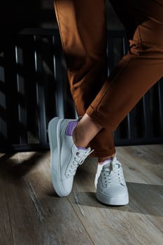 Female legs in white leather sneakers with perforations. Collection of summer women's shoes. White women's sneakers with laces