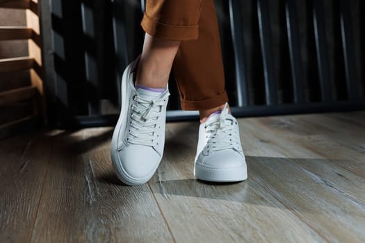 Female legs in white leather sneakers with perforations. Collection of summer women's shoes. White women's sneakers with laces