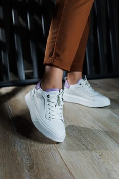 Female legs in white leather sneakers with perforations. Collection of summer women's shoes. White women's sneakers with laces