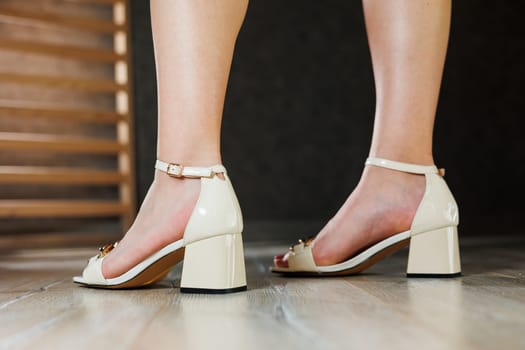 Beautiful slender legs of a girl in leather sandals on high heels on the floor against gray parquet. Collection of women's sandals