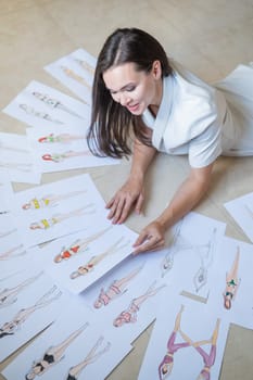 A woman lies on the floor and looks at sketches of swimwear and underwear