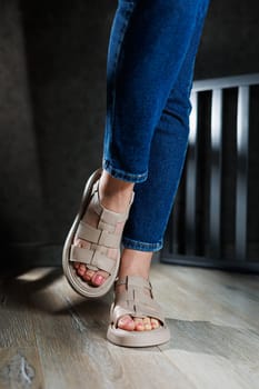 Collection of women's leather summer sandals. Slender female legs in beige leather sandals without heels.