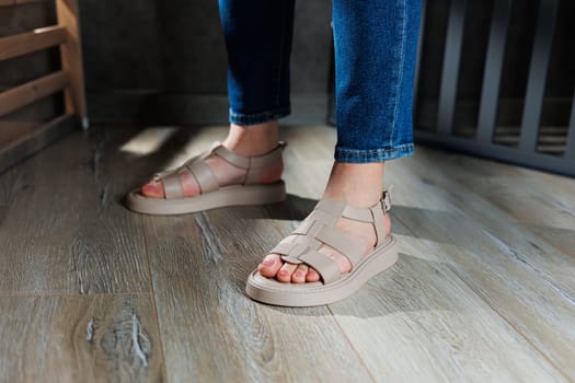 Collection of women's leather summer sandals. Slender female legs in beige leather sandals without heels.