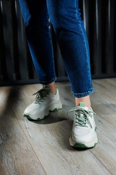 White leather summer sneakers on female legs in jeans. Women's casual sneakers. Comfortable women's shoes