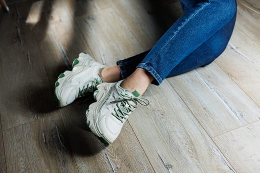 Sports shoes for women. Slender female legs in jeans and white stylish casual sneakers. Comfortable women's summer shoes. Casual women's fashion.