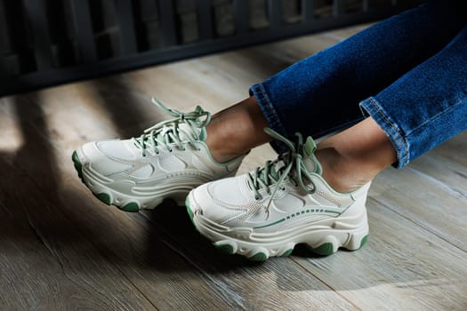 Sports shoes for women. Slender female legs in jeans and white stylish casual sneakers. Comfortable women's summer shoes. Casual women's fashion.