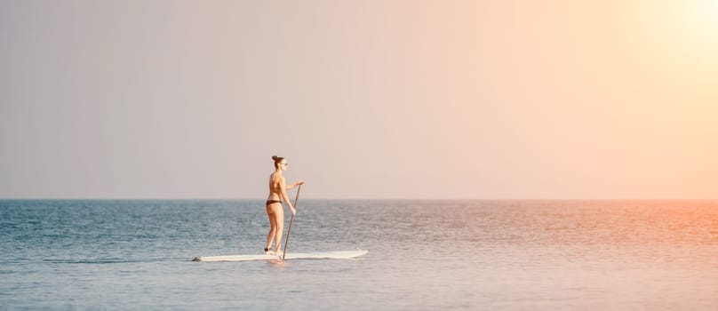 Silhouette of woman standing, surfing on SUP board, confident paddling through water surface. Idyllic sunset or sunrise. Sports active lifestyle at sea or river.