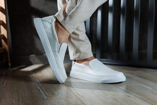 Close-up of male feet in white casual shoes. Fashionable young man standing in leather stylish white moccasins in fashionable trousers. Seasonal summer men's shoes. Casual street style.