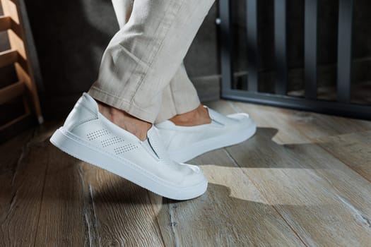 Close-up of male feet in white casual shoes. Fashionable young man standing in leather stylish white moccasins in fashionable trousers. Seasonal summer men's shoes. Casual street style.