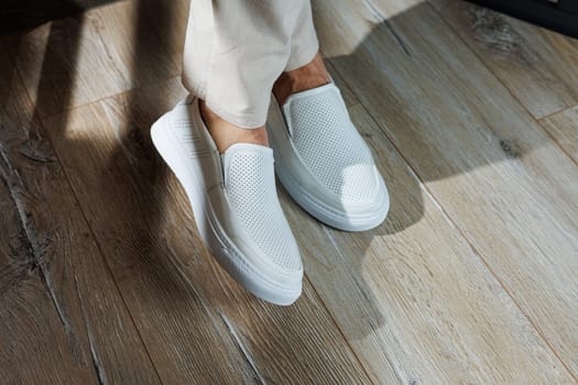 Close-up of male feet in white casual shoes. Fashionable young man standing in leather stylish white moccasins in fashionable trousers. Seasonal summer men's shoes. Casual street style.