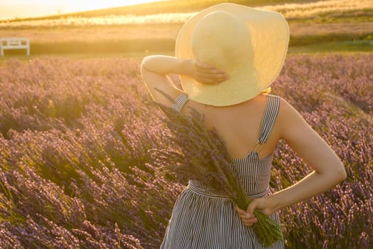 Woman in a straw hat enjoying the view of a lavender field in the light of sunset.