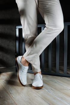 Male feet close-up in white casual shoes. Fashionable young man standing in leather stylish white moccasins in trousers. Seasonal summer men's shoes. Casual street style.