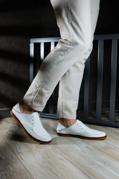 Male feet close-up in white casual shoes. Fashionable young man standing in leather stylish white moccasins in trousers. Seasonal summer men's shoes. Casual street style.