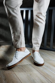 Male feet close-up in white casual shoes. Fashionable young man standing in leather stylish white moccasins in trousers. Seasonal summer men's shoes. Casual street style.