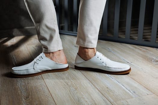 Male feet close-up in white casual shoes. Fashionable young man standing in leather stylish white moccasins in trousers. Seasonal summer men's shoes. Casual street style.