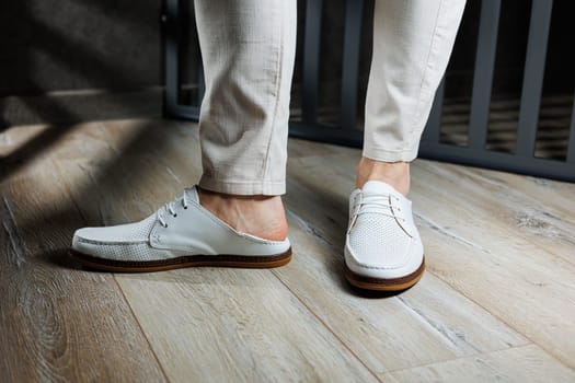 Male feet close-up in white casual shoes. Fashionable young man standing in leather stylish white moccasins in trousers. Seasonal summer men's shoes. Casual street style.