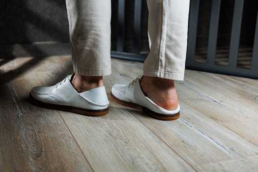 Male feet close-up in white casual shoes. Fashionable young man standing in leather stylish white moccasins in trousers. Seasonal summer men's shoes. Casual street style.