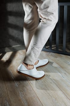 Male feet close-up in white casual shoes. Fashionable young man standing in leather stylish white moccasins in trousers. Seasonal summer men's shoes. Casual street style.