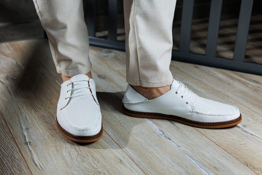 Male feet close-up in white casual shoes. Fashionable young man standing in leather stylish white moccasins in trousers. Seasonal summer men's shoes. Casual street style.