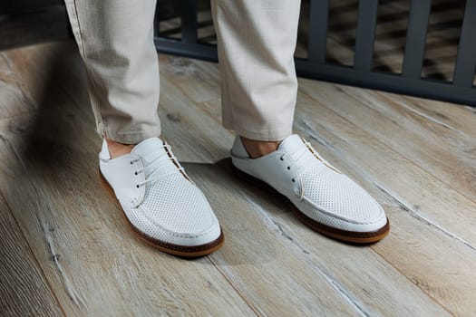 Male feet close-up in white casual shoes. Fashionable young man standing in leather stylish white moccasins in trousers. Seasonal summer men's shoes. Casual street style.
