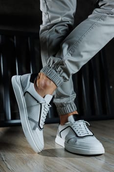 Male legs in white leather summer shoes. Comfortable men's white sneakers with laces. Casual men's sneakers