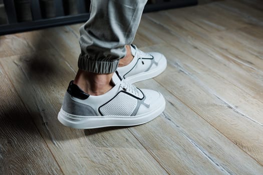 Casual white sneakers for men. Male legs in white leather summer shoes. Comfortable men's white sneakers with laces.