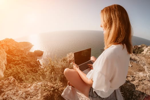 Woman sea laptop. Business woman in yellow hat working on laptop by sea. Close up on hands of pretty lady typing on computer outdoors summer day. Freelance, digital nomad, travel and holidays concept.