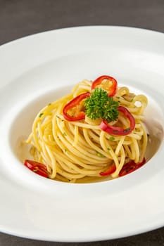 Spaghetti with paprika on white porcelain plate on dark stone table