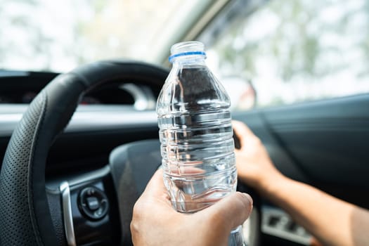 Asian woman driver holding bottle for drink water while driving a car. Plastic hot water bottle cause fire.