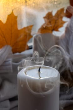 Thanksgiving and Hello Fall Halloween concept Celebrating autumn holidays at cozy home on the windowsill Hygge aesthetic atmosphere Autumn leaves spices and candle on knitted white sweater in warm yellow lights. Still life. Raining Outside