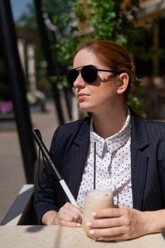 Blind woman in business suit drinking ice coffee in outdoor cafe