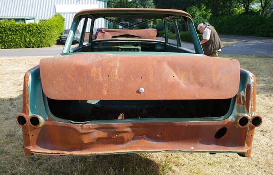 Back of a totally rusted old car with a man in the background photographing it