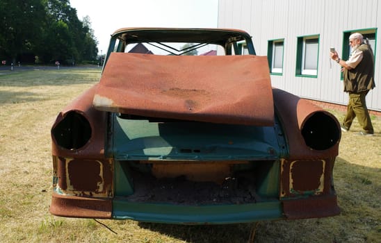 Front of a totally rusted old car with a man in the background photographing it