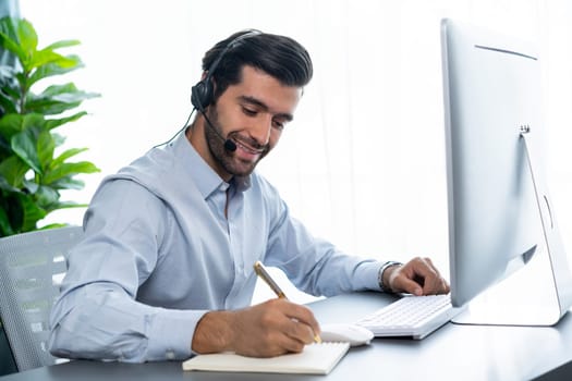 Male call center operator or telesales representative siting at his office desk wearing headset and engaged in conversation with client providing customer service support or making a sale. fervent