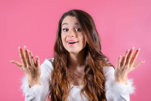 Portrait of a cheerful young woman happily gesturing with her hands on the pink background