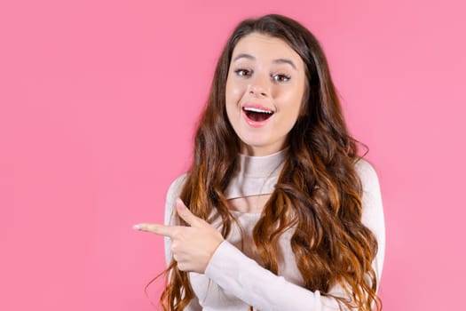 A portrait of a young student pointed by finger on copy space with pink background.