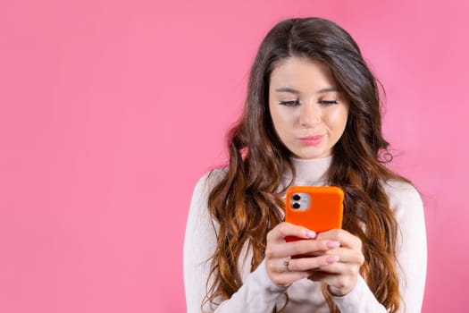 Young woman texting someone unhappily using a smartphone on the pink background.