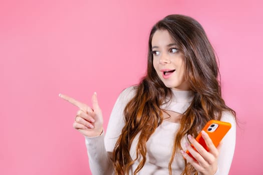 Happy young woman pointed by finger and standing isolated over pink background