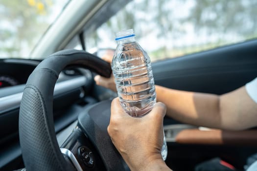 Asian woman driver holding bottle for drink water while driving a car. Plastic hot water bottle cause fire.