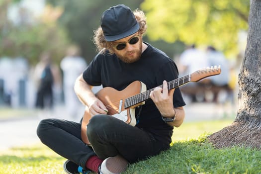 A man wearing hat and sunglasses playing electric guitar in the park. Mid shot