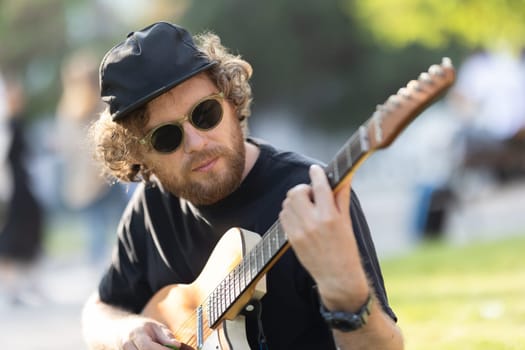 A man wearing hat and sunglasses playing guitar in the park. Portrait