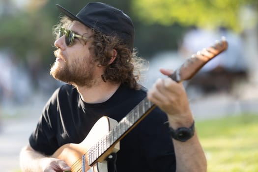 A man hipster wearing hat and sunglasses playing guitar in the park. Portrait